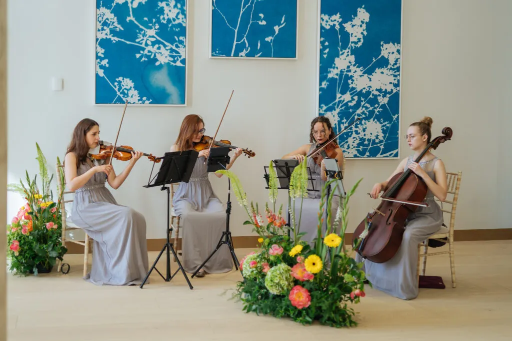 A string quartet performing beside floral arrangements and blue botanical artwork at Herland Gardens.